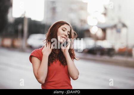 Hübsches Mädchen in Freizeitkleidung spricht auf einem Handy während des Gehens in der Stadt Straße Sonnenuntergang pünktlich. Stockfoto