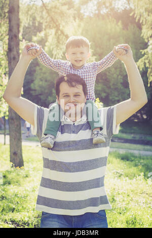 Glücklicher Vater und seinen zwei Jahre alten Sohn auf Papas Schultern im Park bei Sonnenuntergang Stockfoto