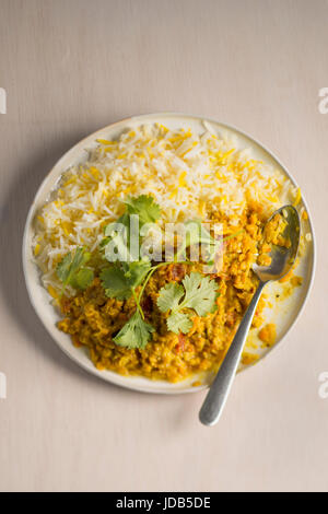 Eine Platte von Vegan-Linsen-Curry mit Basmati-Reis, garniert mit frischem Korianderblätter, auf einem hölzernen Hintergrund mit einem Löffel. Stockfoto