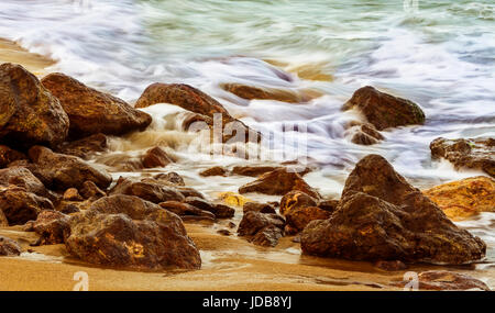 Bunte Langzeitbelichtung seidig glatte Wasser des Meeres über Felsen und Sand am Strand Yarada, Visakhapatnam Stockfoto