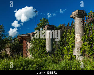 Alten Backstein-Haus mit einem alten Zaun mit Steinsäulen, Stahl Stangen mit Spitzenwerten im Dickicht Bäume, Gras und Büsche im alten park Stockfoto