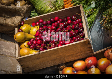 Ein Anzeigefeld von Kirschen und Birnen, umgeben von verschiedenen Obst und Gemüse Stockfoto