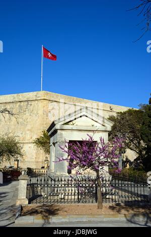 Maltesischer Flagge auf dem Dach St Johns Cavalier Gebäudes mit einer Gedenkstätte im Vordergrund in Hastings Gärten, Valletta, Malta, Europa. Stockfoto