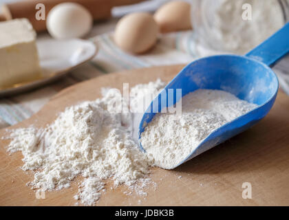Weizenmehl in blauen Plastiklöffel auf Holzbrett mit Backzutaten auf dem Hintergrund Stockfoto