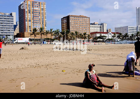 Durban, Südafrika. Eine afrikanische Frau sitzt auf dem Sand in der Nähe des Ufers genießen das warme Wintertag früh Stockfoto