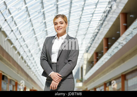 Porträt von überzeugt junge Geschäftsfrau posiert, Blick in die Kamera in modernen Bürogebäude unter Glasdach Stockfoto