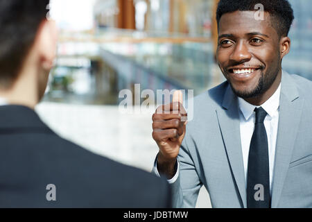 Porträt des jungen erfolgreicher afrikanisch-amerikanischer Geschäftsmann lächelnd und Daumen auftauchen, während im Gespräch mit Partner feiern viel moderne Office-build Stockfoto