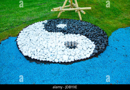 Zeichen von Yin Yang aus schwarzen und weißen Steinen auf einem grünen Rasen verlegt Stockfoto