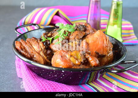 Huhn mit Pflaumen gekocht im Ofen in einer schwarzen Schale auf einem Textil-Hintergrund Stockfoto