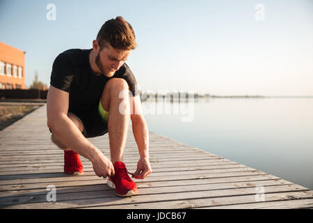 Porträt eines Mannes binden Schnürsenkel auf Sportschuh beim laufen am Strand am Morgen Stockfoto