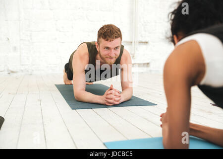 Bild der Gruppe von fröhlichen multiethnischen Menschen im Yoga-Studio. Blick auf einander und in Plank. Stockfoto