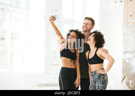 Multikulturelle Gruppe von Freunden in Sportbekleidung machen Selfie auf Handy drinnen stehen Stockfoto