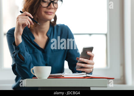 Bild einer lächelnden Frau in Gläsern am Cafétisch halten Handys und Notizen im Editor abgeschnitten Stockfoto