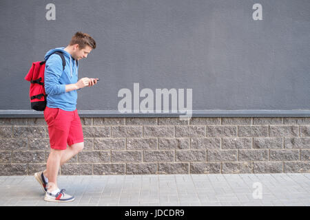 Voller Länge Seite Porträt des lächelnden Menschen zu Fuß mit Rucksack auf Hintergrund der schwarzen Wand Stockfoto