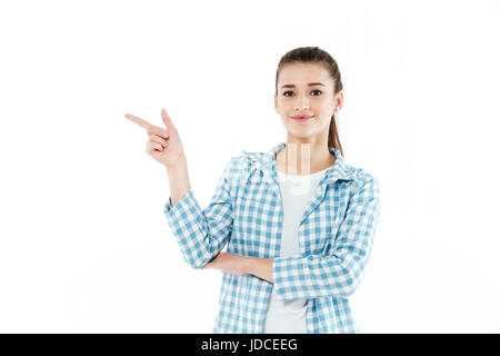 Lächelnde Mädchen trägt kariertes Hemd zeigt mit Finger auf textfreiraum isoliert auf weiß Stockfoto