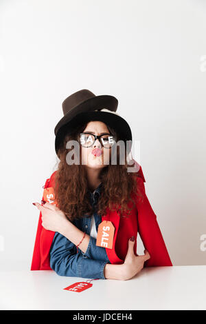 Bild der hübschen jungen Frau, gekleidet in eine Menge Kleidung und Hüte tragen einer Brille mit Verkauf Text auf objektive am Tisch über weiße bac isoliert Stockfoto