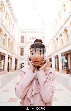 Hübsches Mädchen mit Kopfhörern Musik hören und im freien wegsehen erstaunt Stockfoto