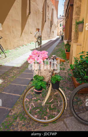 Alghero Sardinien Straße, ein Fahrrad mit rosa Blumen gelegen in einer engen Straße in der historischen Altstadt von Alghero, Sardinien. Stockfoto