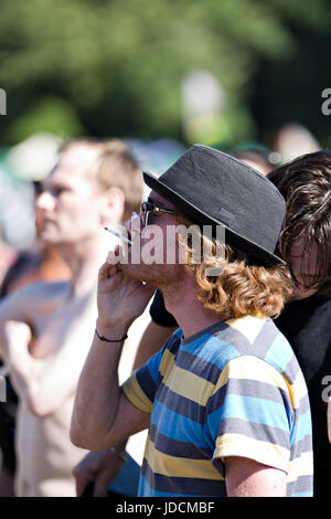 Ein Mann mit Ingwer Haare und trägt einen Hut, rauchte eine Zigarette bei einem Outdoor-Musik-festival Stockfoto