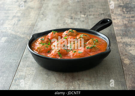 Hackfleischbällchen mit Tomatensauce in Eisenpfanne auf Holztisch. Stockfoto
