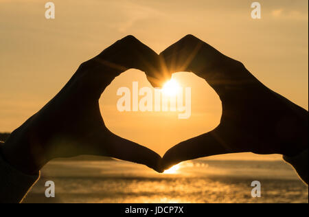 Hand Herz Rahmen Form Silhouette gegen die Sonne & Himmel von Sonnenauf- und Sonnenuntergang an einem einsamen Strand leer gemacht Stockfoto