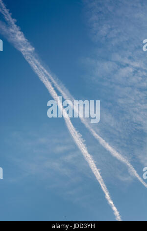 Zwei diagonal Chem-Trails von Flugzeugen in den blauen Himmel mit Wolken Stockfoto