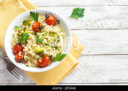 Bulgur mit Gemüse: Tomaten, Brokkoli und Petersilie auf weißem Holz Hintergrund - gesunde hausgemachte Bio Vegan vegetarische Ernährung Lebensmittel Stockfoto