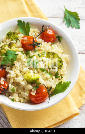 Bulgur mit Gemüse: Tomaten, Brokkoli und Petersilie auf weißem Holz Hintergrund - gesunde hausgemachte Bio Vegan vegetarische Ernährung Lebensmittel Stockfoto