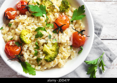 Bulgur mit Gemüse: Tomaten, Brokkoli und Petersilie auf weißem Holz Hintergrund - gesunde hausgemachte Bio Vegan vegetarische Ernährung Lebensmittel Stockfoto