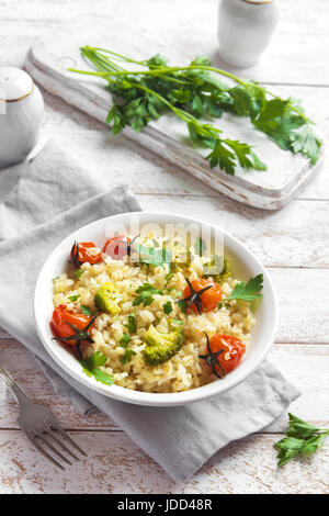 Bulgur mit Gemüse: Tomaten, Brokkoli und Petersilie auf weißem Holz Hintergrund - gesunde hausgemachte Bio Vegan vegetarische Ernährung Lebensmittel Stockfoto