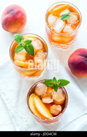 Pfirsich Eistee. Eistee mit Pfirsich Scheiben, Minze und Eiswürfel auf weißem Hintergrund hautnah. Hausgemachte erfrischendes Sommergetränk. Stockfoto