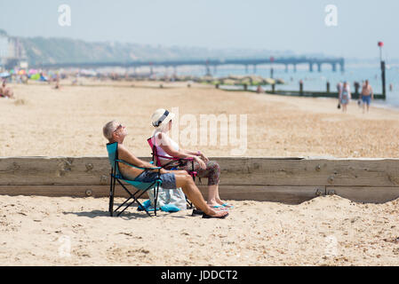 Reifes Paar sitzen in Liegestühlen oder Liegen am Bournemouth, Dorset an einem heißen und sonnigen Sommern Tag Stockfoto