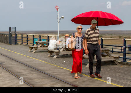 Holz- Picknick Tische & Stühle mit roten Sonnenschirme in Southport, Merseyside, UK. UK Wetter. 20 Juni, 2017. Leichte Winde und lückenhafte Wolken auf Southport Meer als pier Kinderwagen die Meeresbrise aus der Irischen See genießen. Vereinzelt Wolken geben etwas Entlastung von den hohen Temperaturen, als Urlauber und Touristen die Promenade die längste Eisen Pier in Großbritannien. Stockfoto