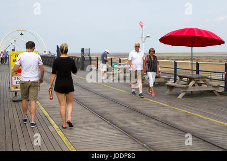 Holz- Picknick Tische & Stühle mit roten Sonnenschirme in Southport, Merseyside, UK. UK Wetter. 20 Juni, 2017. Leichte Winde und lückenhafte Wolken auf Southport Meer als pier Kinderwagen die Meeresbrise aus der Irischen See genießen. Vereinzelt Wolken geben etwas Entlastung von den hohen Temperaturen, als Urlauber und Touristen die Promenade die längste Eisen Pier in Großbritannien. Stockfoto