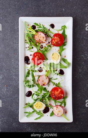 Frische Radieschen, Kirschtomaten, Wachtelei, Parmeggiano mit Balsamico-Glasur auf einem weißen Teller. Mediterranes Lebensgefühl. Gesunde Ernährung. Stockfoto