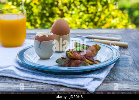 Weich gekochtes Eiern mit Speck Avocado Soldaten auf dem Tisch im Garten Stockfoto