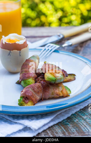 Weich gekochtes Eiern mit Speck Avocado Soldaten auf dem Tisch im Garten Stockfoto