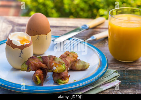 Weich gekochtes Eiern mit Speck Avocado Soldaten auf dem Tisch im Garten Stockfoto