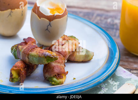 Weich gekochtes Eiern mit Speck Avocado Soldaten auf dem Tisch im Garten Stockfoto