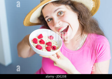 Lächelnde Frau halten gesund und natürlich Frühstück, Haferflocken und Himbeeren in eine Schüssel geben Stockfoto
