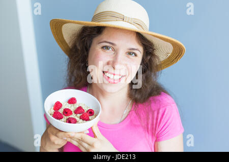 Lächelnde Frau halten gesund und natürlich Frühstück, Haferflocken und Himbeeren in eine Schüssel geben Stockfoto