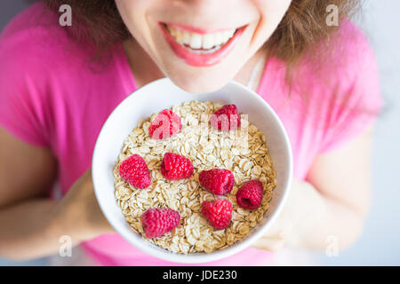 Lächelnde Frau halten gesund und natürlich Frühstück, Haferflocken und Himbeeren in eine Schüssel geben Stockfoto
