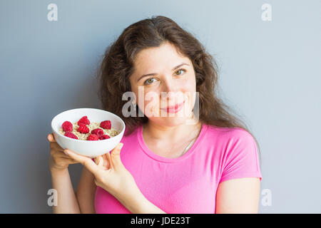 Lächelnde Frau halten gesund und natürlich Frühstück, Haferflocken und Himbeeren in eine Schüssel geben Stockfoto