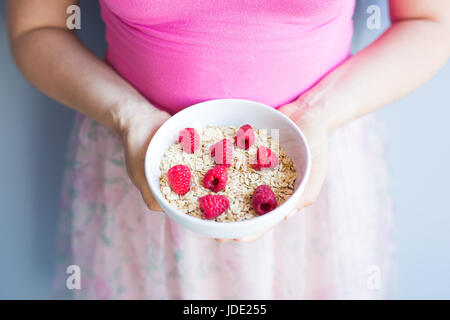 Frauenhand halten gesund und natürlich Frühstück, Haferflocken und Himbeeren in eine Schüssel geben Stockfoto