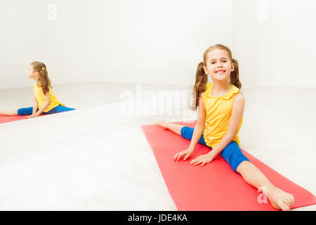 Porträt von lächelndes Mädchen Durchführung Seite geteilt, sitzen auf Yoga-Matte in hellen Fitnessraum Stockfoto