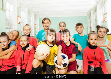 Gruppe der Fußballmannschaft, preteen Jungs und Mädels, sitzen zusammen im Turnsaal Stockfoto