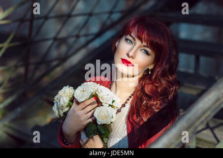 Schöne junge Frau in roten Wollschal sitzt auf alten Haus Treppe mit Blumen. Frühherbst. Außerhalb Schuss. Umgebungslicht. Closeup Portrait. Kopieren s Stockfoto