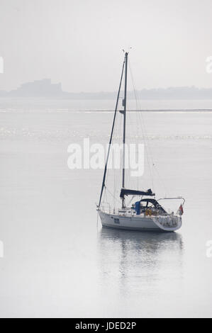 Yacht vor Anker vor heiligen Insel mit Bamburgh Castle im Hintergrund Stockfoto