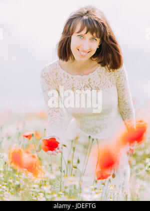 Das Close-up Portrait der lächelnde Braut berühren die Mohnblumen im Feld Stockfoto