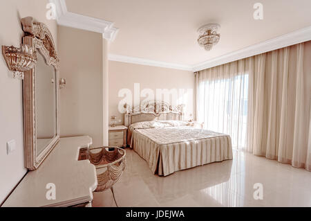 Luxuriöses Schlafzimmer in Pastellfarben im neoklassizistischen Stil, mit einem großen Bett und einem Frisiertisch mit Marmorböden ausgestattet. Stockfoto